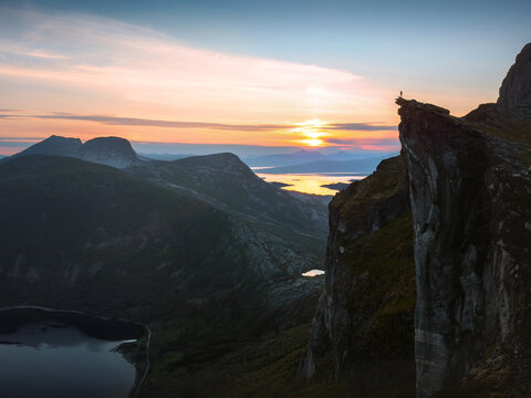 Kjerna cliff at sunset in Norway with lone hiker on the rock edge overlooking aerial mountains scenery, travel extreme adventure outdoor active vacations freedom exploration mountaineering solo