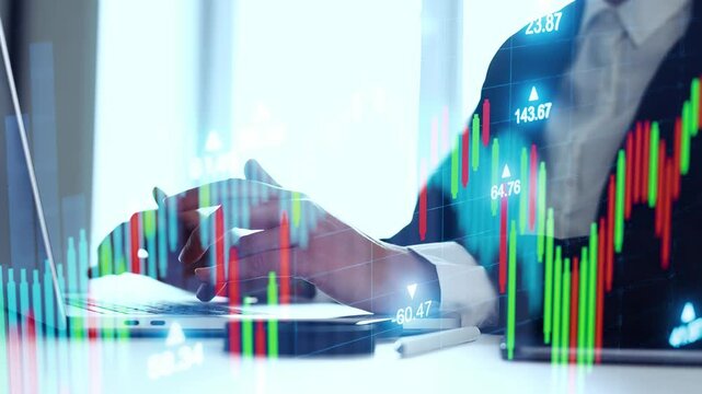 A person is working on a laptop while analyzing stock market data. Financial graphs show upward and downward trends. The setting is likely an office environment during daylight.