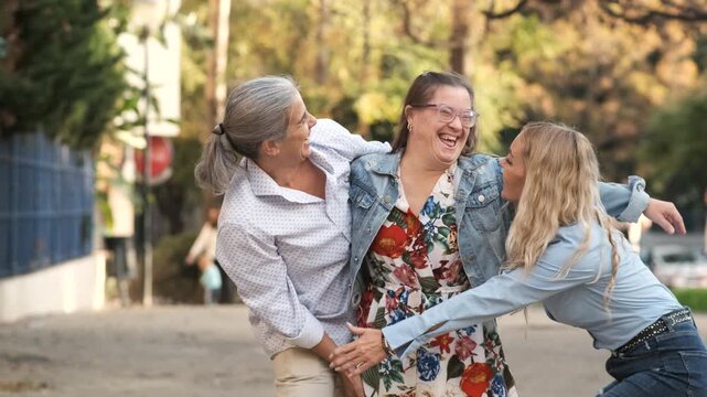 Authentic moment of a happy mother embracing her two adult daughters. One daughter has Down syndrome, enjoying a beautiful day outdoors