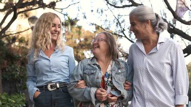 Slow motion of happy mature women and female friend with Down syndrome walking in park against blurred background during daytime