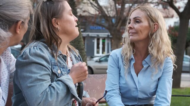Slow motion of happy mature woman with Down syndrome talking with female friends sitting on bench in city park during daytime