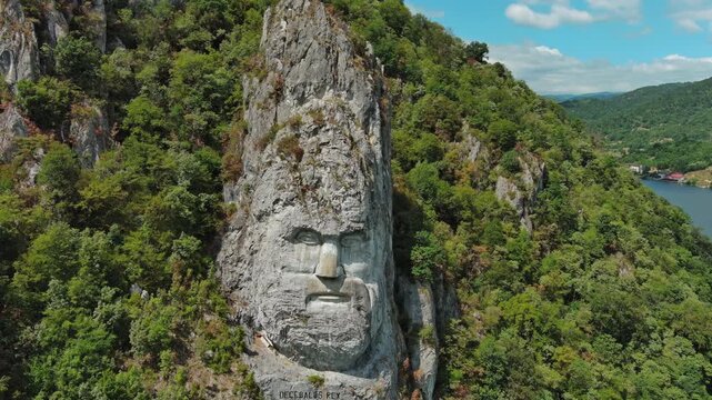 Aerial around view of stone carved statue portrait of ancient dacian king Decebal. Sculpture located on shore of Danube River, Romania, 4k