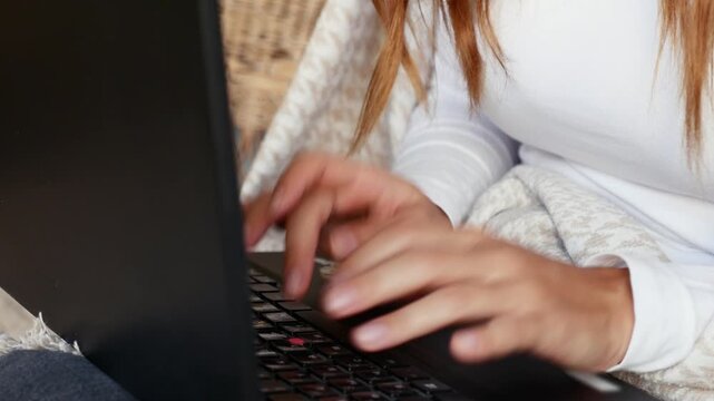 Close-up of woman using laptop while working remotely from home in cozy environment