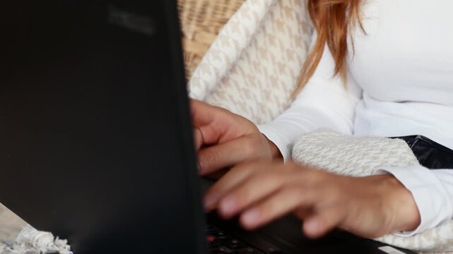 Close-up of woman typing on laptop while working from home under cozy blanket