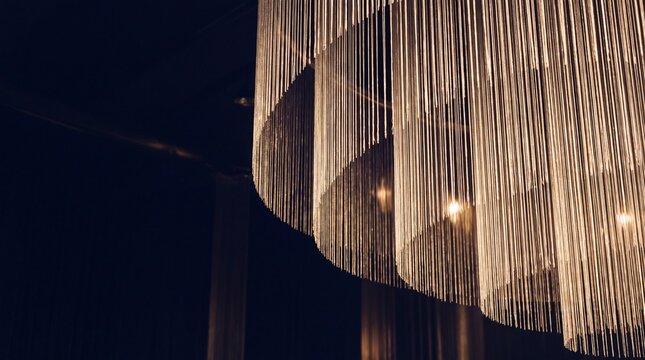 Modern metallic fringe chandelier with warm spotlight illumination against dark interior background