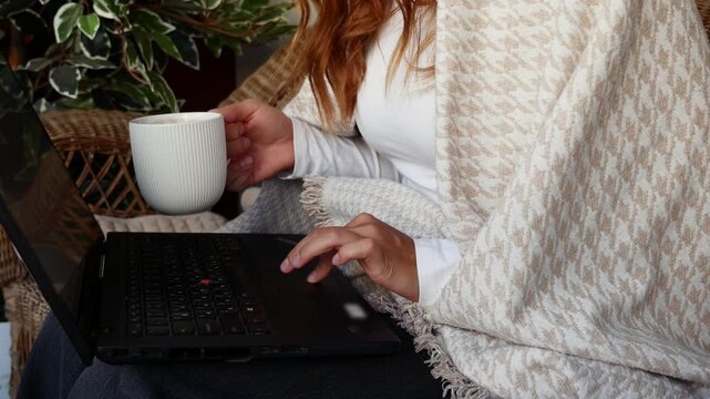 Close-up of woman working on laptop and drinking coffee while working from home on balcony