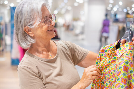 Senior woman with gray hair smiling while shopping for new colorful clothing in a modern fashion retail store, enjoying leisure and consumerism activities