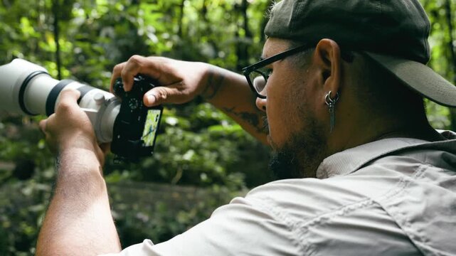 Young latino wildlife photographer using a professional camera with a telephoto lens to shoot in a lush rainforest in Costa Rica