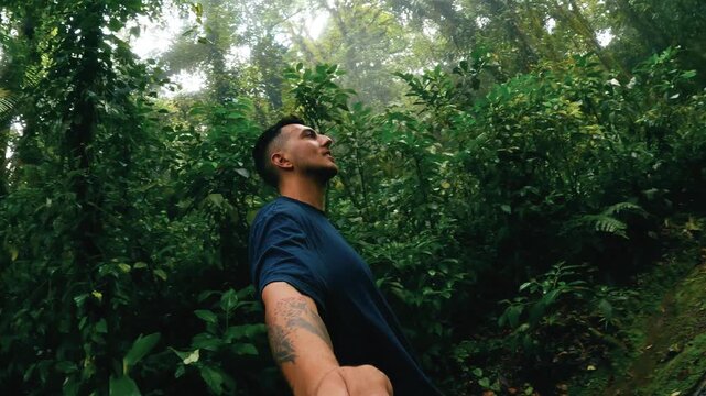 Young tattooed man taking a selfie video, smiling and walking on a path in the lush jungle of Arenal Volcano National Park, Costa Rica