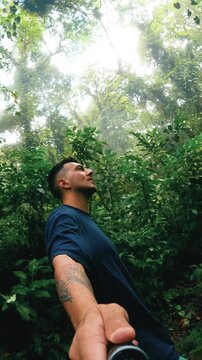 Happy man with a tattoo filming himself with a selfie stick while walking through a lush jungle path in the Arenal Volcano National Park