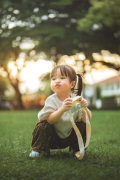 Curious toddler girl holding toy camera while sitting on grass in green park at sunset, enjoying outdoor exploration, imaginative play, childhood discovery, creativity.