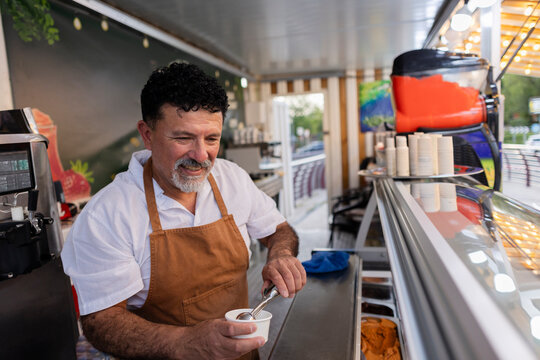 Mature man scooping delicious gelato into cup