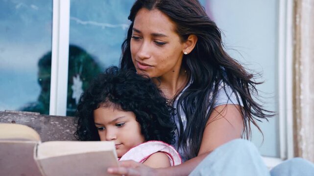 Caring latina mother reading a book with her cute daughter. Woman and little girl enjoying a story together, bonding in a peaceful moment