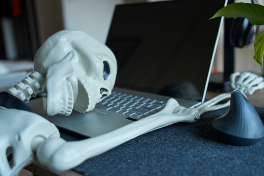 Skeleton collapsed with head resting on laptop keyboard at office desk