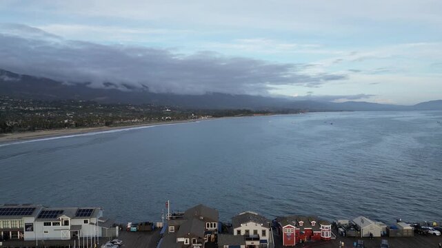Drone shot moving backwards over Stearns Wharf off a beach on a rainy dusk early evening in Santa Barbara, California after a recent rain in January 2024.