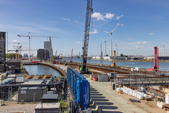 Antwerp, Belgium - 06 September 2026: Massive construction works for the Oosterweel link next to water, with cranes, tanks, and wind turbines.