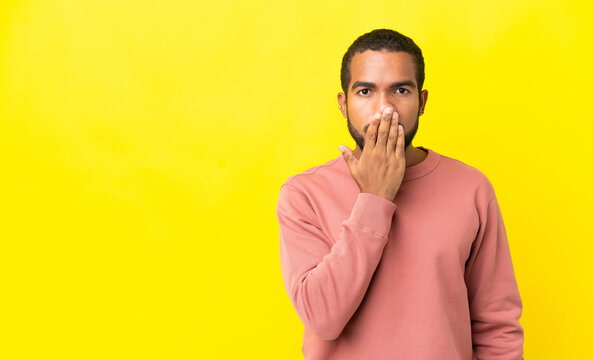 Young latin man isolated on yellow background covering mouth with hand
