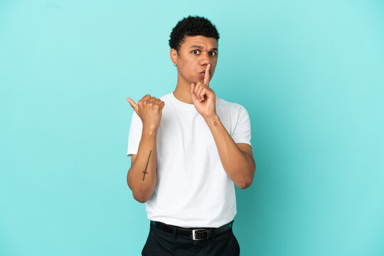 Young African American man isolated on blue background pointing to the side and doing silence gesture