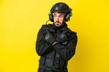 Fototapeta premium SWAT caucasian man isolated on yellow background pointing to the laterals having doubts