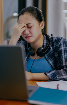 Tired young Asian woman feel pain eyestrain rubbing dry irritated eyes fatigued from computer work. Stressed female suffer from headache bad vision sight problem sit at home table and using laptop.