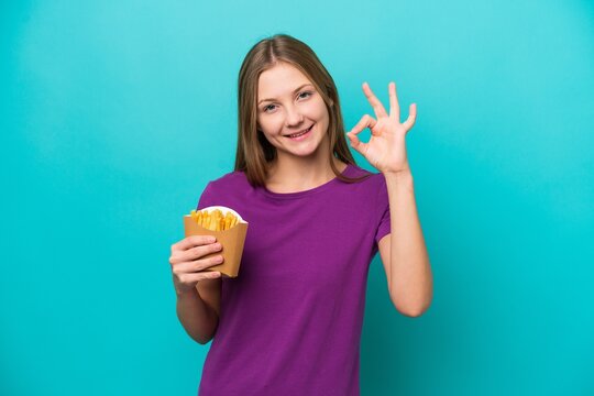 Young Russian woman catching french fries isolated on blue background showing ok sign with fingers