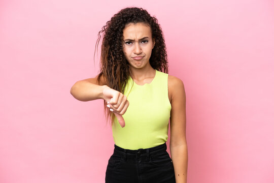 Young hispanic woman isolated on pink background showing thumb down with negative expression