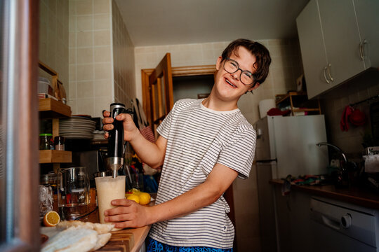 Smiling teenage boy with Down syndrome using hand blender while preparing breakfast at home