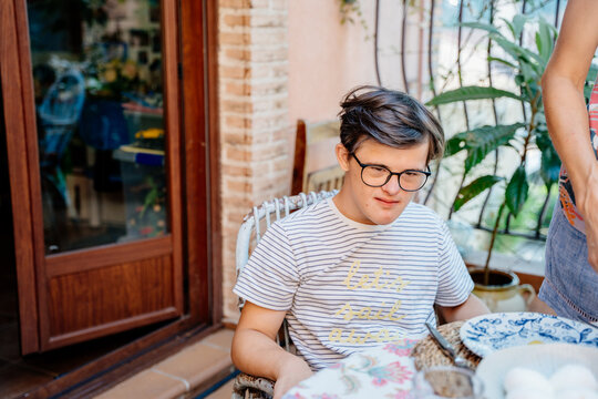 Teenage boy with Down syndrome waiting at outdoor family breakfast table on sunny home terrace