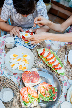 Mother helping teenage son with Down syndrome prepare open sandwich during family breakfast