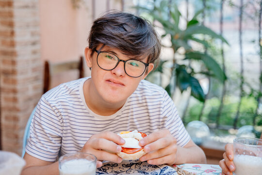 Teenage boy with Down syndrome holding breakfast sandwich during relaxed family meal outdoors