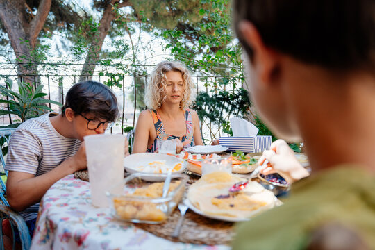 Mother and two sons sharing relaxed outdoor breakfast together on leafy Mediterranean terrace