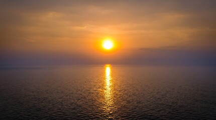 Fototapeta premium Golden sun setting over a calm ocean with a bright reflection on the shimmering water surface