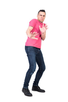 Full body male in pink t shirt and jeans making protective gesture and cringing face in disgust