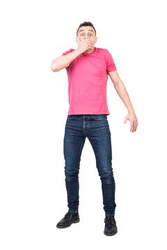 Full body man in casual clothes looking at camera with shock and covering mouth after accidentally telling secret