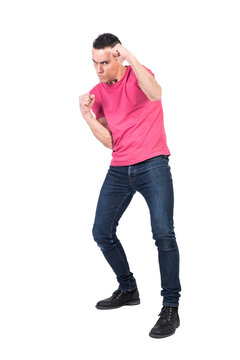 Full body of serious young male fighter in casual outfit looking at camera seriously while standing in boxing stance with clenched fists