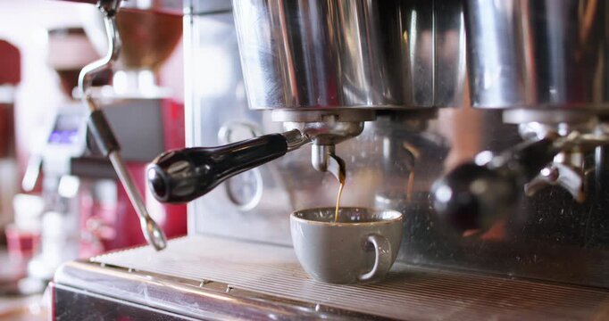 Preparing espresso shot. Professional coffee maker. Brown aroma drink brewing on cafeteria equipment pouring in cup from metal horn.