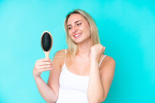 Young caucasian woman with hair comb isolated on blue background celebrating a victory
