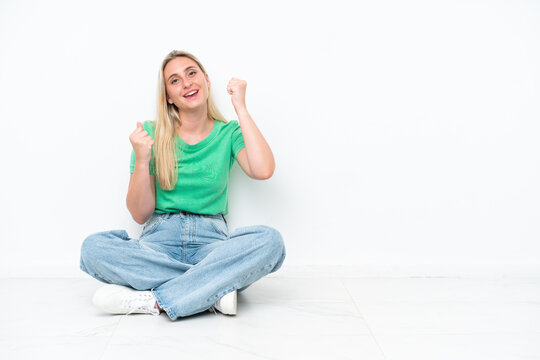 Young caucasian woman sitting on the floor isolated on white background celebrating a victory