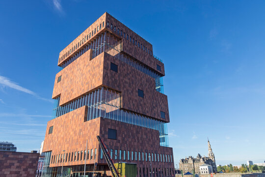 Antwerp, Belgium - 06 September 2026: The iconic Museum aan de Stroom (MAS) building featuring modern red Indian sandstone and curved glass architecture under a bright blue sky.