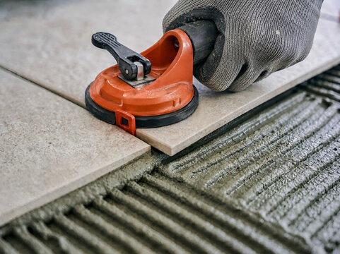 Tile installer laying ceramic floor tile with suction cup tool