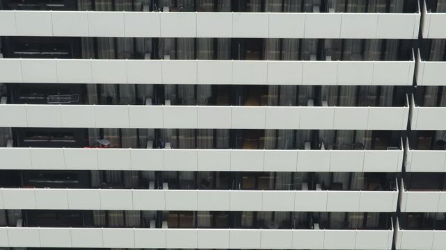 Repetitive stacked residential balconies on highrise facade with pale panelled fronts and dark glass sliding doors, captured from frontal view
