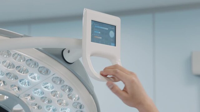 Medical worker adjusts the touchscreen controls of a surgical light inside a modern operating room. Hospital technology, surgery preparation, clinical equipment, healthcare innovation and professional