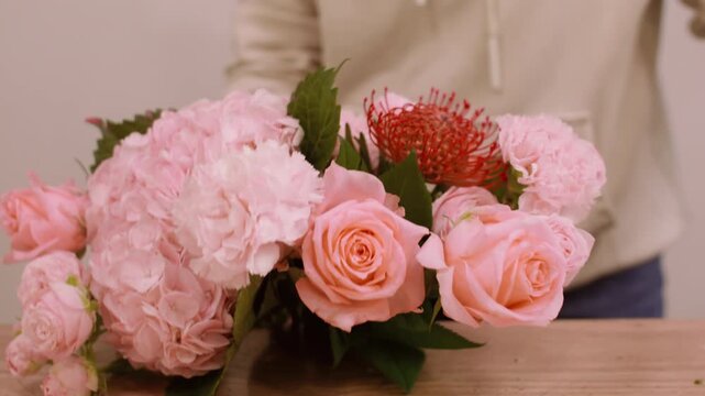 Floral composition. Florist bouquet. Unrecognizable female arranging pink color roses hydrangea fresh flowers on wooden table.