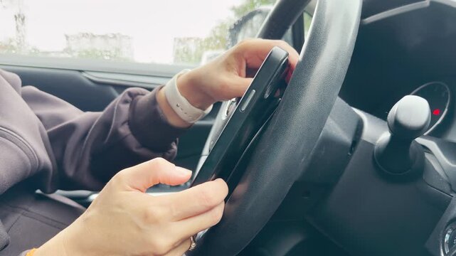 Hands hold a smartphone near a car steering wheel. A driver checks messages during a rainy wait. The quiet moment feels calm yet slightly impatient.