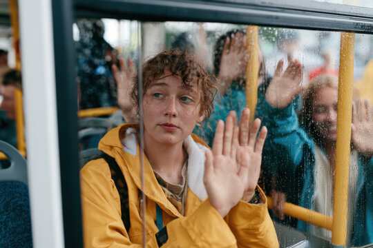 Young woman with curly hair looking out bus window on a rainy day