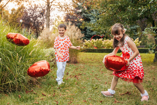 Children Play With Red Heart-Shaped Decorations in a Garden During Summer, Celebrating Love and Friendship on Valentine's Day