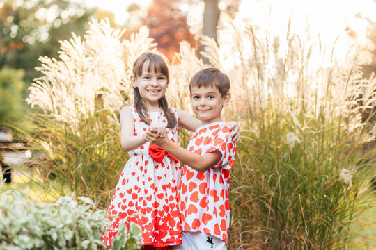 Two Children Stand Together in a Field, Holding Hands and Wearing Outfits With Red Hearts During Summer Days Filled With Love