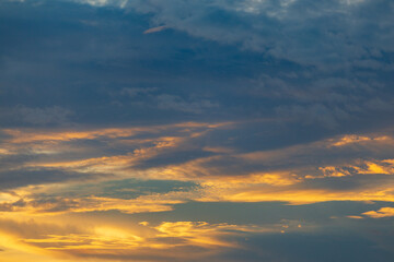 Obraz premium Dramatic sunset sky with golden and dark blue clouds creating a beautiful natural spectacle