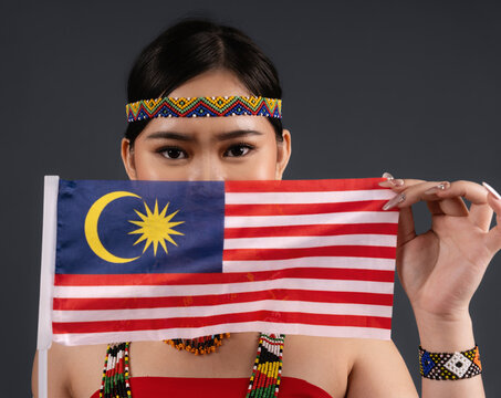Young Woman in Traditional Murut Tahol Simba Costume Covering Face with Flag of Malaysia