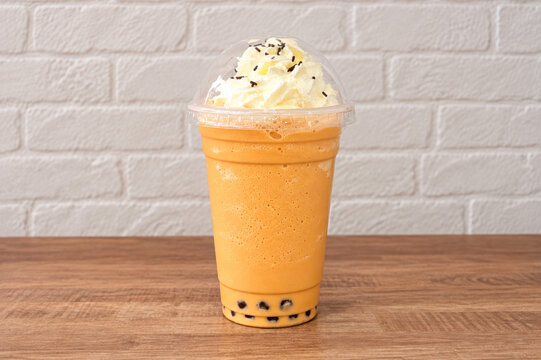 A high-quality photo mock-up of Thai bubble tea in a clear plastic cup with a domed lid, filled with creamy iced tea with black tapioca pearls, on a kitchen counter